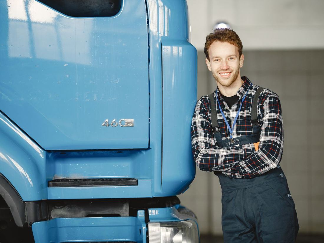 The owner of a vehicle workshop standing beside a truck, arms folded, in his own garage.